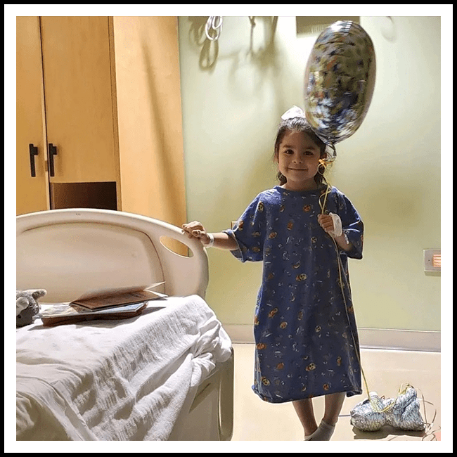 A little girl in a hospital room holding onto a mirror