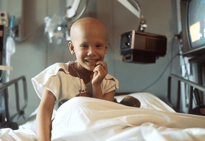 A young boy in hospital bed smiling for the camera.