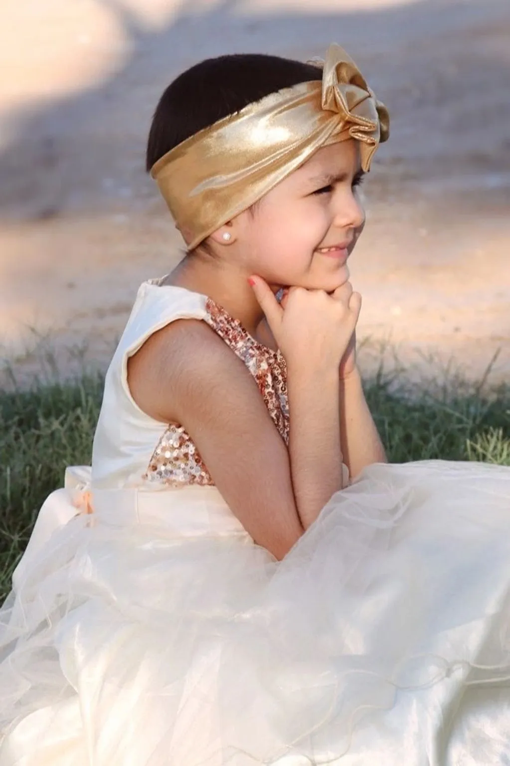 A little girl in a gold dress sitting on the grass.